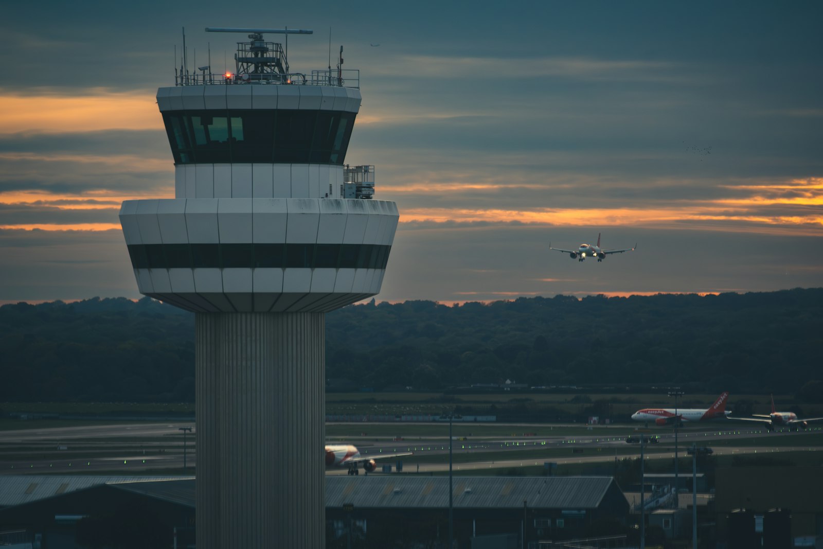 Torre di controllo aeroportuale al tramonto con aereo in avvicinamento